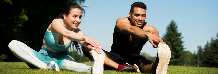 Two people are seen stretching their legs on a grassy field.